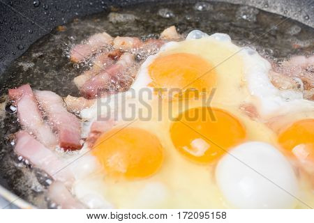 Frying eggs with sliced bacon in the hot oil.