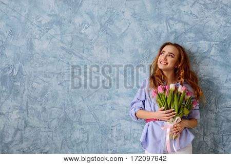 beautiful young girl with bouquet of tulips on the blue wall background. Wide shot with copy space