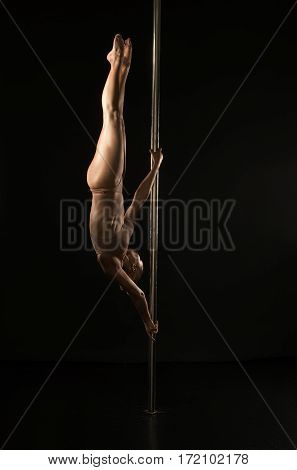 Young woman in beige lingerie with shiny gold skin hanging upside down on pylon in studio