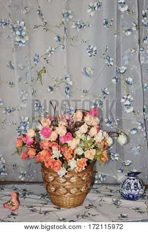 beautiful multi-colored artificial roses in a wicker basket on the background fabric folds with embroidery