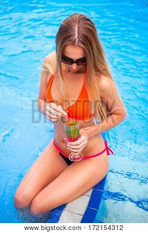 Young Pretty Blond Woman In A Orange Bikini And Sunglasses Enjoying Cocktail In A Swimming Pool