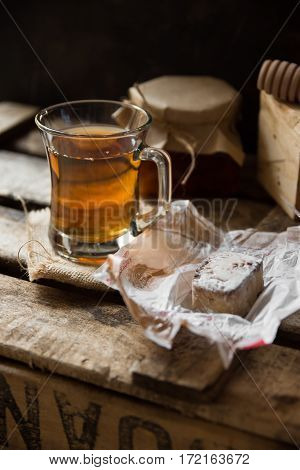 Glass cup with hot tea with jar of honey or jam wood spoon Spanish cookie polvoron on vintage box black wall backgroundrustic countryside interiorcozy atmosphere
