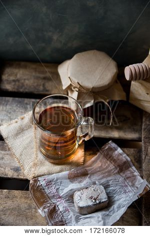 Glass cup with hot tea with jar of honey or jam wood spoon Spanish cookie polvoron on vintage box grey wall background rustic vintage interior cozy atmosphere top angle view