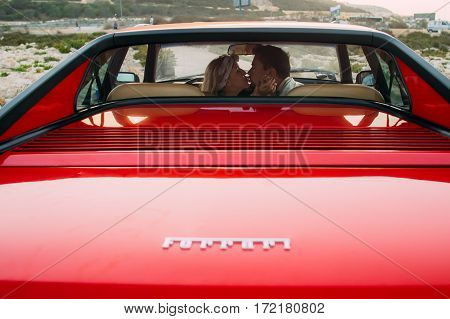 Young Girl In White Dress And Man Kissing On The Front Seats Of The Red Ferrari