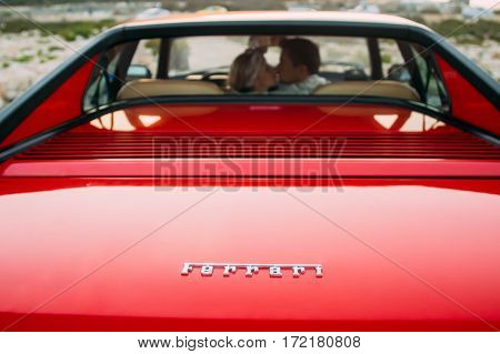 Young Girl In White Dress And Man Kissing On The Front Seats Of The Red Ferrari