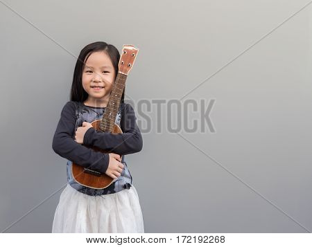 Little Asian Child Play The Ukulele, Gray Background