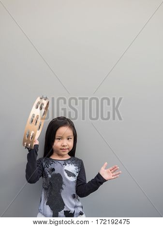 Little Asian Child Play The Tambourine, Gray Background