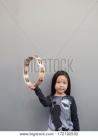 Little Asian Child Play The Tambourine, Gray Background