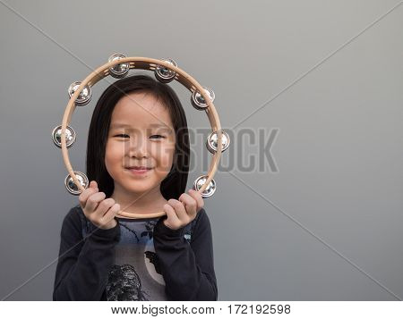 Little Asian Child Play The Tambourine, Gray Background