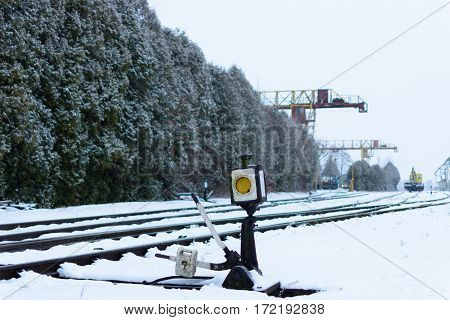 Rail switch (Hand rail shooter) in the snow. Railway. 
In the background gantry cranes.