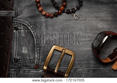 The objects of everyday life, men jeans, belt, watch, bracelets on hand. Flat top view. Men's fashion, casual outfits with accessories