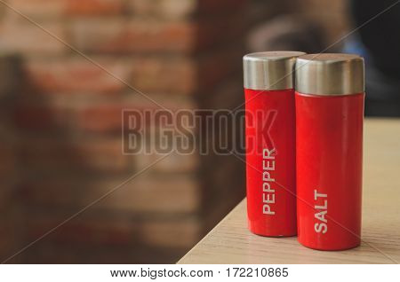 Red plastic salt cellar and pepperbox on a wooden table on loft brickwall background faded colors