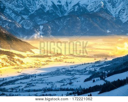 Morning in alpine valley. Winter haze illuminated by ray of rising sun, Leogang, Austria.