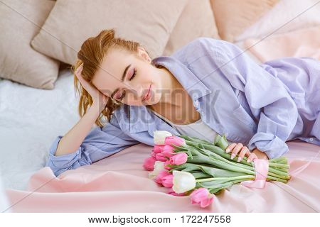 beautiful young girl with bouquet of pink and white tulips lying on the bed
