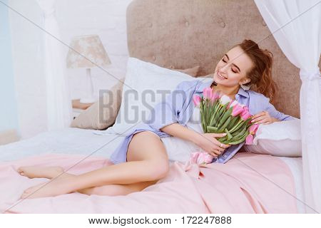 beautiful woman with white and pink tulips smiling on the bed