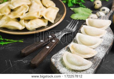 Dumplings with potatoes in plate on black background. On board cooking raw dumplings with potatoes. Ingredients for dumplings with potatoes onions arugula eggs bay leaf potatoes sour cream sauce.