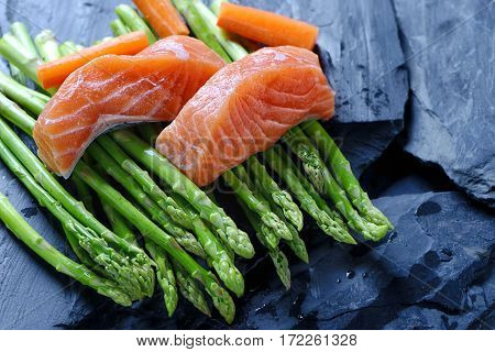 Salmon and aspargus on a black stone background.