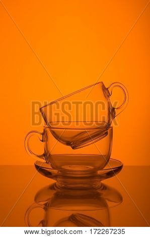 Two transparent glass cups on orange background