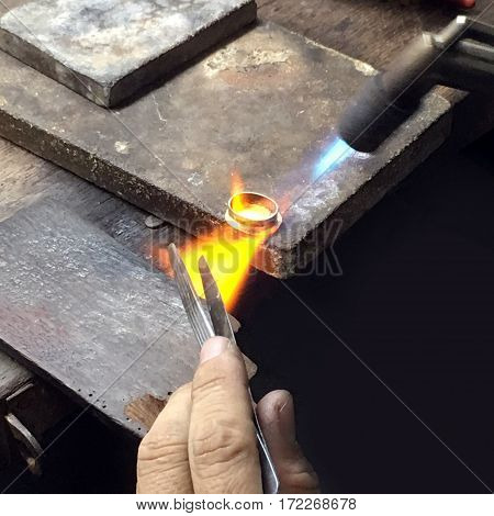 A gold making worker is firing on the gold ring to adjust its shape