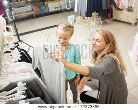 Child with mother in a children's store. Happy girl choosing clothes. Family are shopping