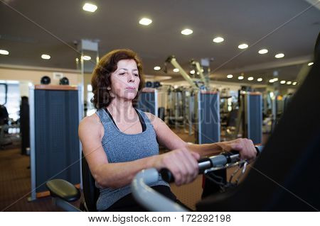 Beautiful fit senior woman in sports clothing in gym doing cardio workout, exercising on recumbent bicycle. Sport fitness and healthy lifestyle concept.