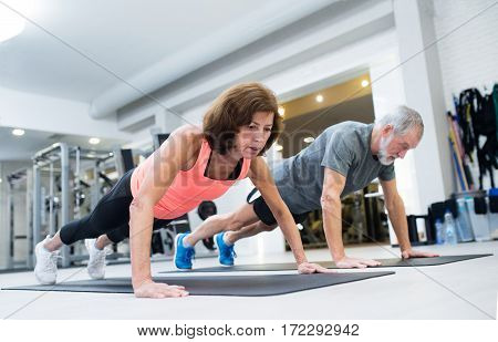 Beautiful fit senior couple in gym working out, doing push ups.