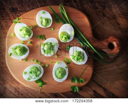 Deviled eggs appetizer with avocado on cutting board. Top view.