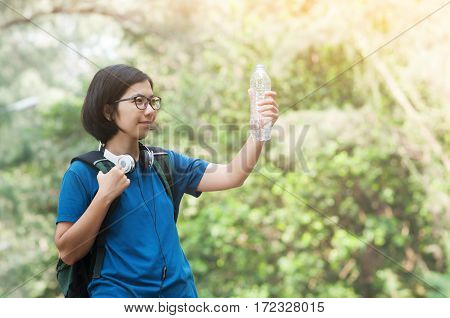 Asian woman hiker with backpack wear headphone holding bottle of water on nature background. copy space.