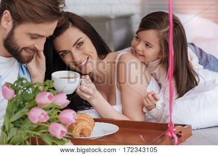 Pleasant morning time. Cheerful happy attractive woman holding a cup and drinking coffee while enjoying her breakfast