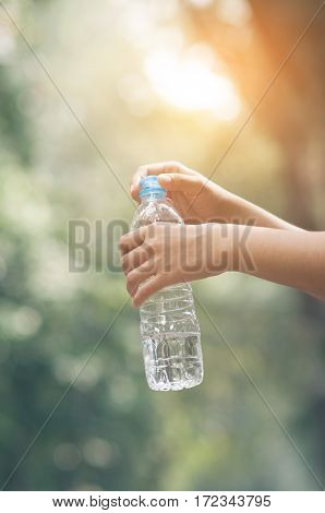 Close up Asian woman hand holding bottle of water on nature background. copy space. Traveler.
