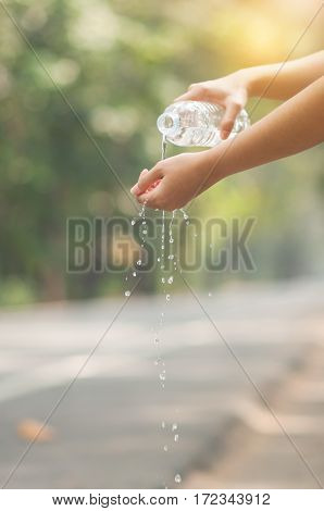Close up Asian woman hand pouring water from bottle on hand with nature background. copy space. Traveler.