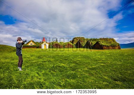 The elderly woman photographed the old village. Ethnographic Museum-estate Glaumbaer, Iceland. The concept of the historical and cultural tourism