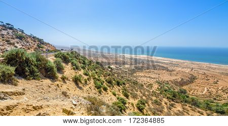 Beautiful view on oceanic beach from a high hill in Morocco in summer. Road serpentine goes towards the ocean. Panorama shot