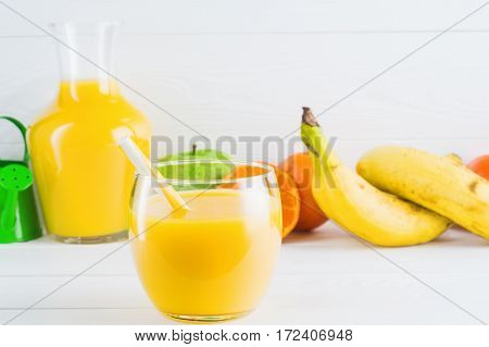 A glass of fresh orange juice and fruits orange tangerine apple banana on white wooden background with copy space. Healthy lifestyle and diet concept. Healthy eating for weight loss.