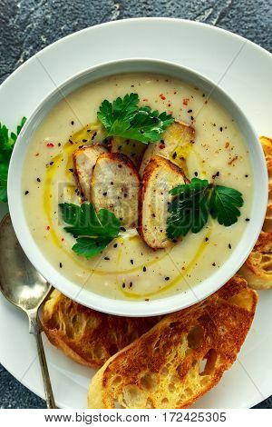 Creamy chicken soup with vegetables in bowl with chiabatta toast, parsley and nigela seeds sprinkle on stone table.