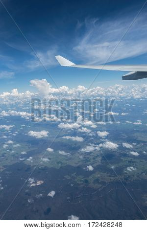 Plane flying high above the clouds. Some hills and vegetation can be seen below.