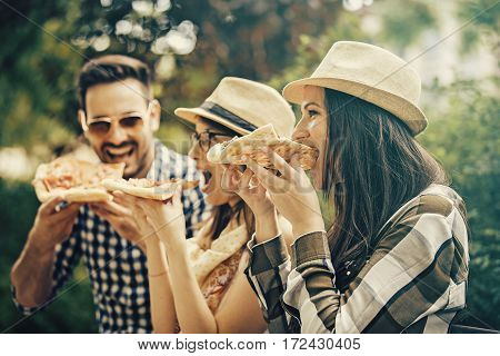 Group of young people having fun in the park and eating pizza.