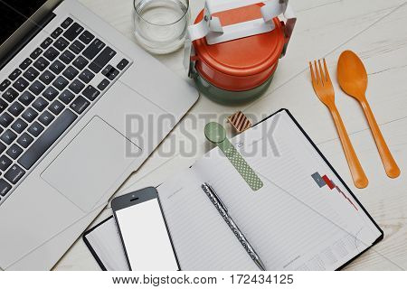 Fast lunch break in the office with colored asian styled food containers and typical business accessories - laptop cell and diary