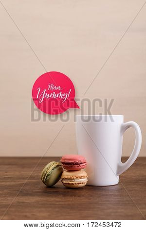 Macaroon cakes. Mockup white tea or coffee cup. Yummy speech bubble. Almond sweet cookies. Wooden rustic board.