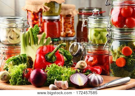Jars With Marinated Food And Raw Vegetables On Cutting Board
