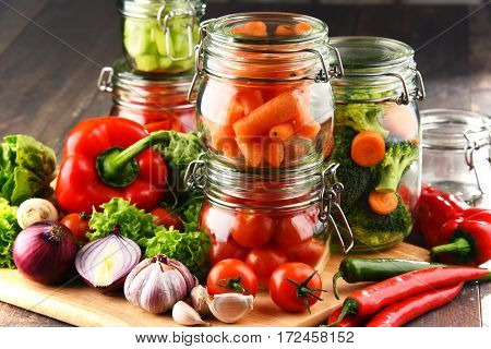 Jars With Marinated Food And Raw Vegetables On Cutting Board