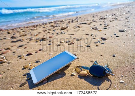 Mobile cell phone and car keys on beach sand as a Vacation metaphor