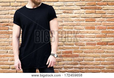 Closeup view of bearded muscular man wearing black tshirt and jeans posing outside. Empty brown grunge brick wall on the background. Hotizontal mockup
