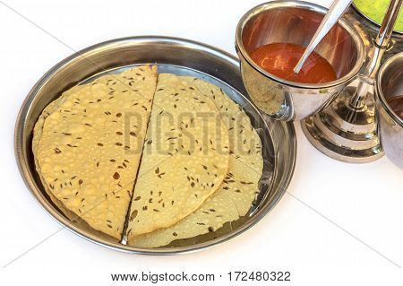 Indian bread served with the traditional assortment of sauces, in the typical tableware, on a white background. Selective focus