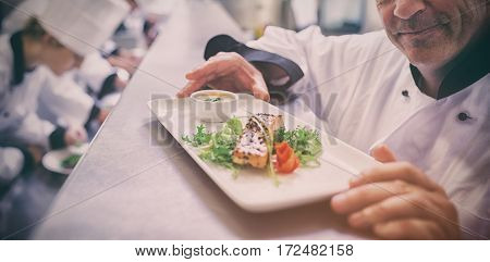 Head chef happy with finished salmon dish with trainees working in kitchen