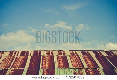 Old rusted and weathered steel quonset hut roof against a blue sky with fluff clouds vintage tone