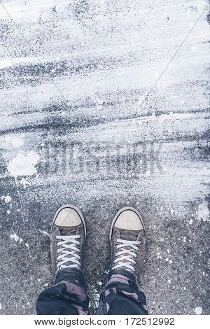 Standing on concrete floor with white drybrush stains male feet in worn sport shoes on the street
