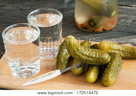 Pickled cucumbers and shot glass of vodka on wooden background. Rustic style. Selective focus