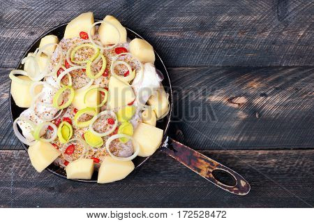 Chicken legs with potato leek chilli and spices in a frying pan on a wooden background. Raw fresh ingredients for baking. Rustic style. Top view
