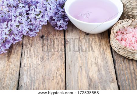 Spa background with blossoming lilac flowers bowl with aroma oil or flower hydrolat and sea salt. Copy space